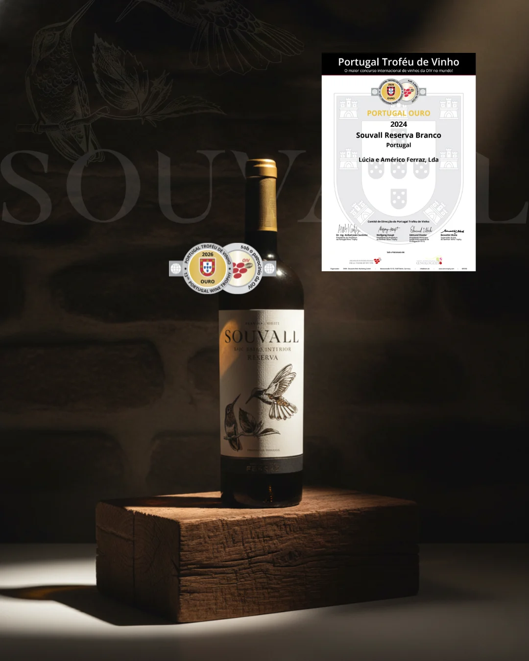 Garrafa de vinho Souvall Reserva Branco com ilustração de colibri no rótulo, iluminada sobre bloco de madeira rústica, exibindo o certificado e a medalha de Ouro Portugal Ouro 2026.