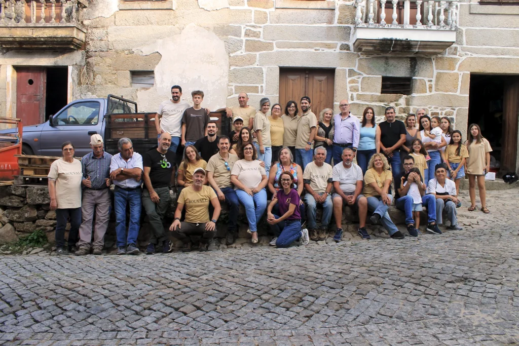 Fotografia de grupo da Família Ferraz e da equipa de trabalhadores reunidos em frente a casas de pedra tradicionais na festa de encerramento da vindima em Vale Flor.